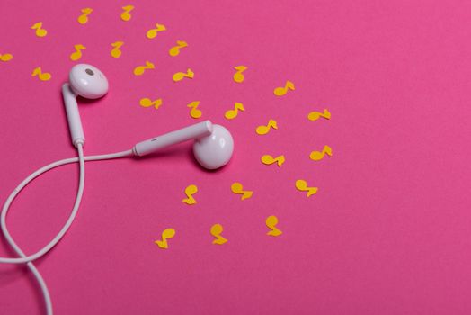 white earphones and yellow paper notes on pink background. view from above