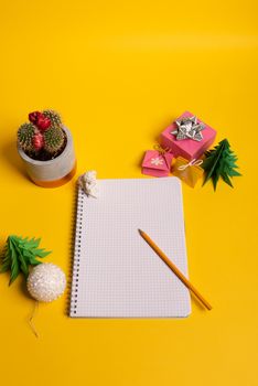 gift box and green origami trees with notepad on yellow desk, table