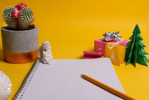 gift box and green origami trees with notepad on yellow desk, table