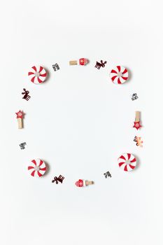 Simple Christmas composition. Round frame of clothespins, candy-bulbs, deer confetti and gifts on white background, copy space. Vertical. Minimal style. Top view. For social media, greeting card.