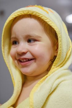 Adorable baby girl sitting under a hooded towel after bath.