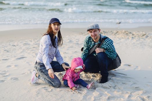 Happy mother, father and daughter in the park. Beauty nature scene with family outdoor lifestyle. Happy family resting together on the green grass, having fun outdoor. Happiness and harmony in family life.