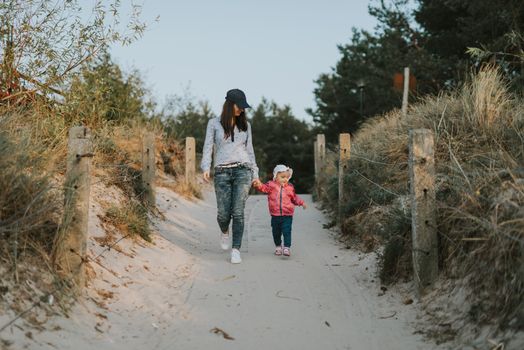 Mother and little daughter walking on the beach.