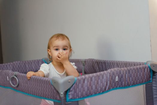 Little baby in a cot. Portrait child baby close up. 18 month old baby girl stands in the crib.