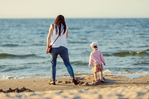 Mother and little daughter walking on the beach.