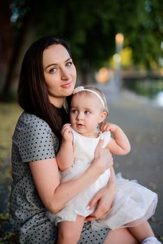 Happy mother and daughter in the park. Beauty nature scene with family outdoor lifestyle. Happy family resting together on the green grass, having fun outdoor. Happiness and harmony in family life.