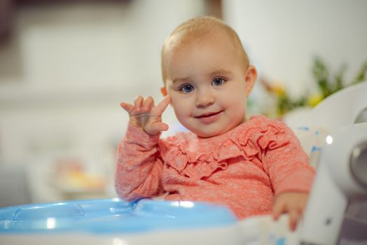 cute blond child sits in a children's chair at the kitchen and eat a juicy peach. Little girl with a piercing look.