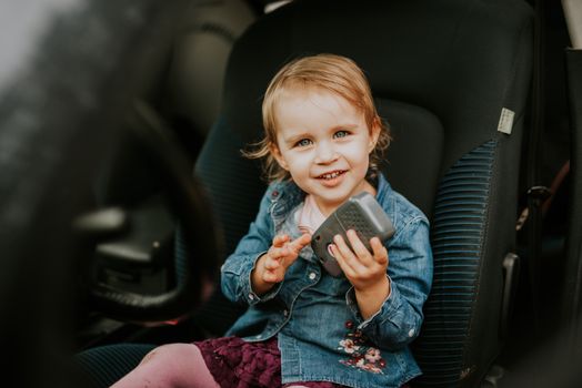 Little girl in a car seat. Holding phone in her hand. Taking driver seat. Car damage. Authentic image.
