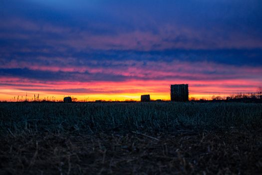 Field with mowed dry grass on the background of an amazing sunset. The grass is collected in haystacks.