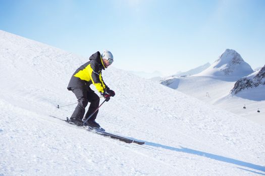 Alpine skier on piste running downhill in beautiful Alpine landscape. Blue sky on background. Free copy space for text