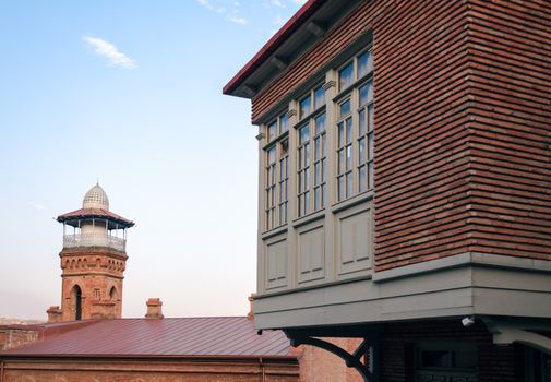 tall old vintage tower and modern brick building with windows on a background of blue sky and clouds in Georgia