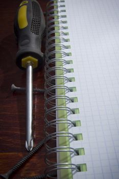 Screwdriver with screws and a squared notebook on the table