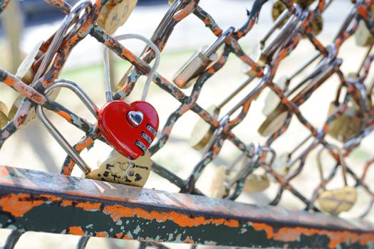 Red heart-shaped combination padlock fastened to metal fence near the Sacre Coeur basilica in Paris, France