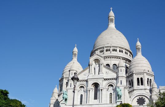 Imposing view of the Basilica of the Sacred Heart of Paris at Montmartre against deep blue sky. Romano-Byzantine architecture constructed in travertine limestone.