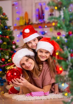 Mom and two daughters lie on the floor of a Christmas tree in the New Year's interior