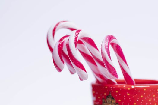 Traditional Christmas candies, lollipop, sticks minimalistic design.New Year candy canes in a red cup on a white background. New Year concept. Sweet candy canes.