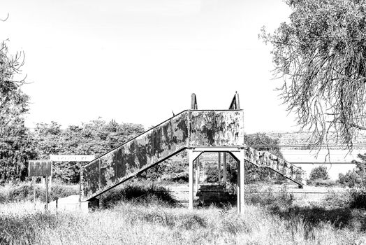 A street scene, with a rusted, old pedestrian railway bridge, in Brandfort in the Free State Province. Monochrome