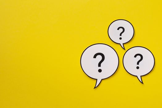 Three speech bubbles with question marks over a bright yellow background with copy space