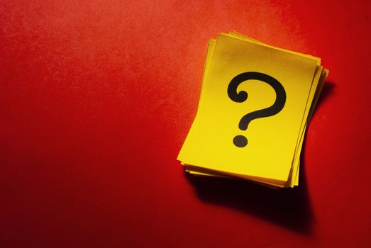 Stack of bright yellow cards with question marks to the side on a festive red background with shadow and copy space
