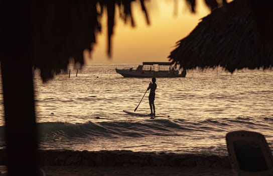 Surfer and ferry behind in the sea at Bayahibe at sunset time