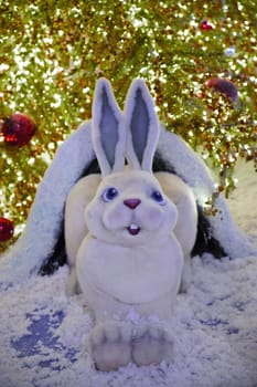 Bright festive illumination. Christmas decoration is a figure of a white hare sitting under a Christmas tree.