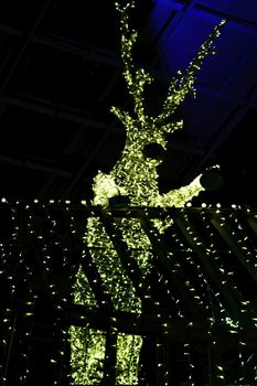 Bright festive Christmas illumination. Glowing figure of a deer against the background of a Christmas tree.