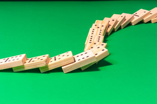 A curved line of dominoes in a domino show has been toppled, with the wooden game pieces cascading across a green surface and lying on top of each other.