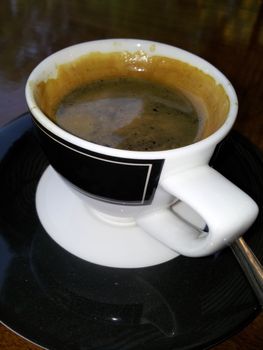 Black coffee in a white cup placed on a black glass table.