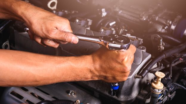 Hand of auto mechanic technician service engine and using wrench socket repairing car in garage
