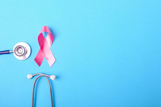 Breast cancer month concept, flat lay top view, pink ribbon and stethoscope on blue background with copy space for your text