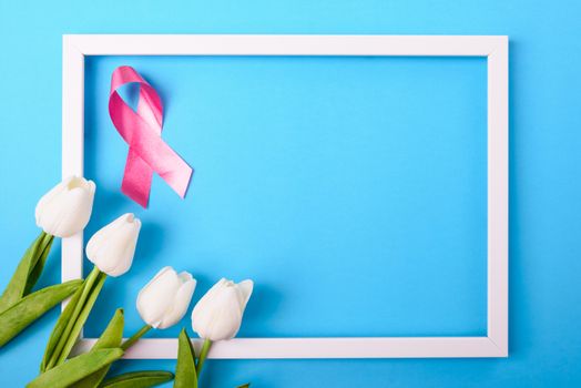 Breast cancer month concept, flat lay top view, pink ribbon and Tulip Flower with photo frame on blue background with copy space for your text