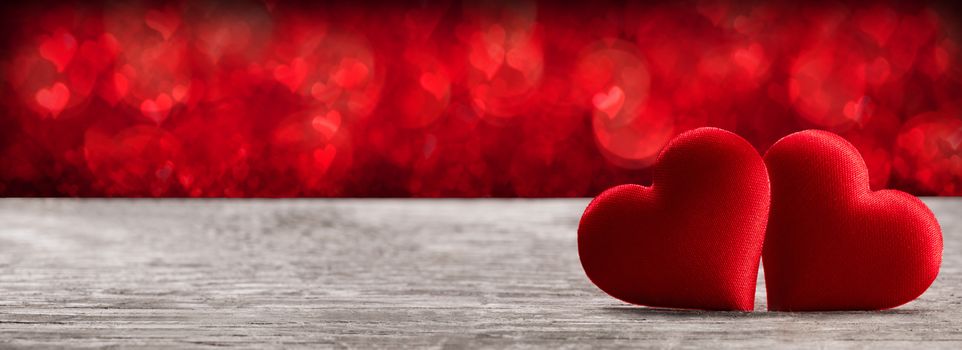 Valentine's day two red silk hearts on wooden background and bokeh lights, love concept