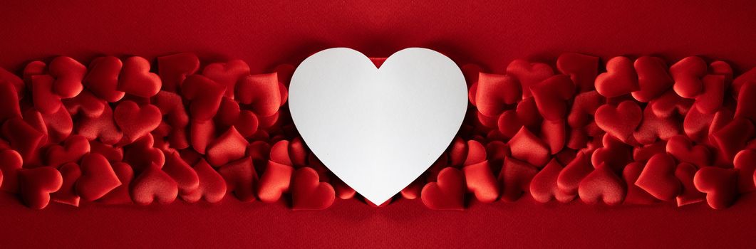 Valentine's day many red silk hearts and white heart shaped paper card background , border frame on red with copy space, love concept