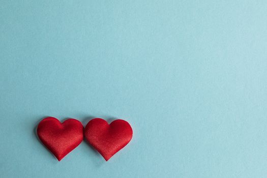 Valentine's day two red silk hearts on blue paper background, love concept