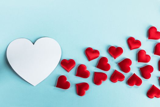 Valentine's day many red silk hearts and white heart shape card on blue paper background , border frame on red with copy space, love concept