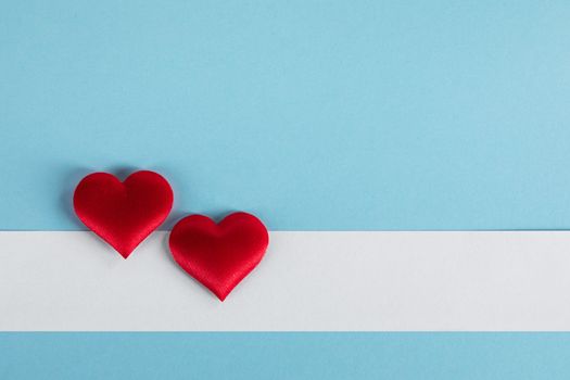 Valentine's day two red silk hearts and white paper on blue paper background, love concept