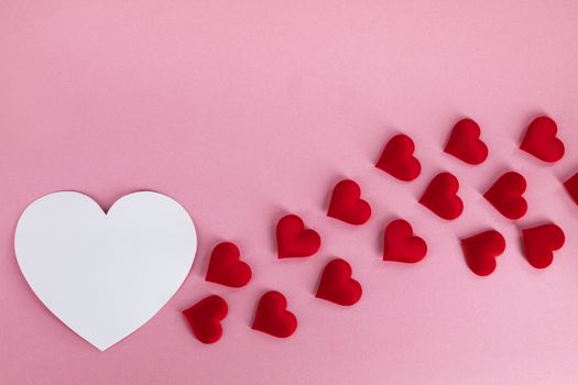 Valentine's day many red silk hearts and white heart shape card on pink paper background , border frame on red with copy space, love concept