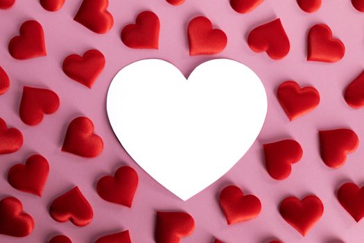 Valentine's day many red silk hearts and white heart shaped card on pink background, love concept