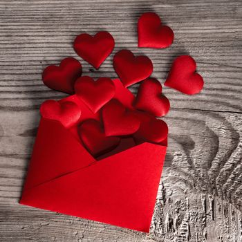 Valentine day love letter, envelope of craft red paper with red hearts heap spread on wood background.
