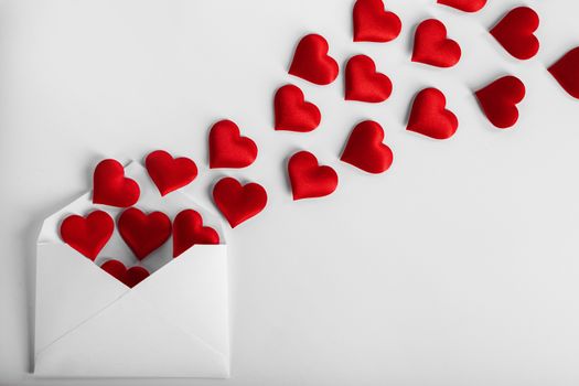 Valentine day love letter, envelope of craft paper with red hearts heap spread on white background.