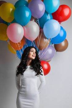 Young pretty woman in white dress with colored balloons on white background with copy space for text