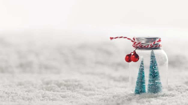 Christmas ornaments of glass jar with striped ribbon , bells and fir trees inside on snow background