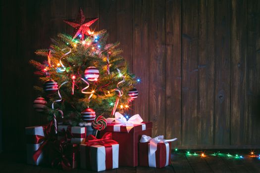 Decorated Christmas tree with glowing lights and gift boxes on wooden background