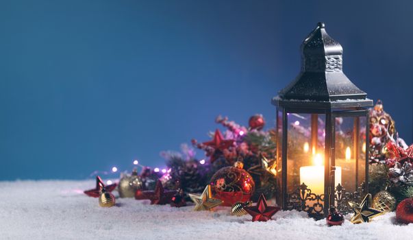 Lantern and red and golden christmas decoration on snow on blue background