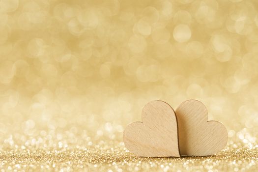 Two small handmade wooden hearts on bright golden lights bokeh background Valentines day card