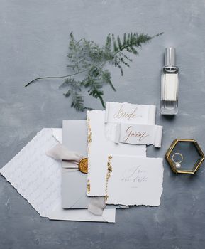 Wedding details flat lay. Wedding invitation and scroll paper. Bottle with fragrance. Simple bouquet. Ring box.