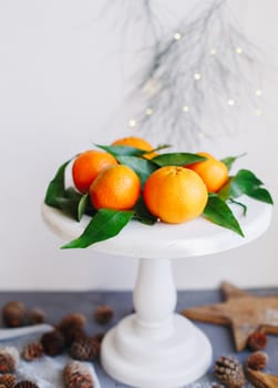 Orange tangerines on grey background in New Year's decor with brown pine cones and green leaves. Delicious sweet clementine. Christmas decoration with mandarins.