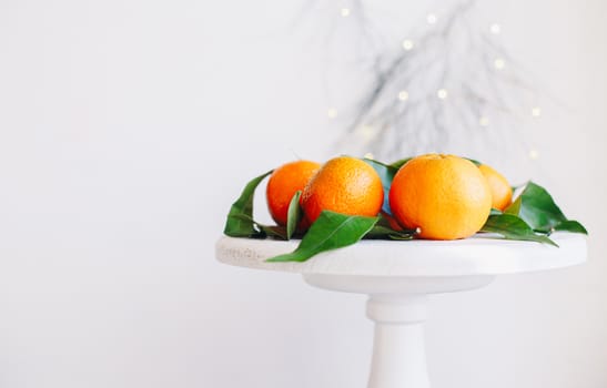 Orange tangerines on grey background in New Year's decor with brown pine cones and green leaves. Delicious sweet clementine. Christmas decoration with mandarins.