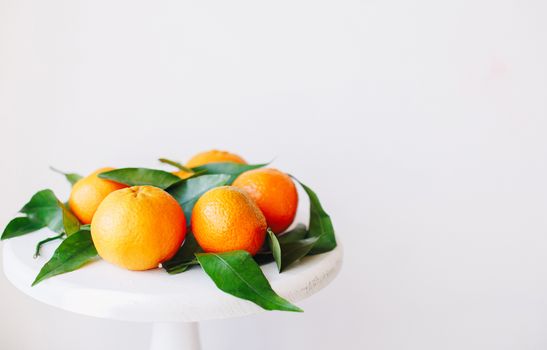 Orange tangerines on grey background in New Year's decor with brown pine cones and green leaves. Delicious sweet clementine. Christmas decoration with mandarins.