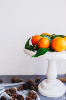 Orange tangerines on grey background in New Year's decor with brown pine cones and green leaves. Delicious sweet clementine. Christmas decoration with mandarins.